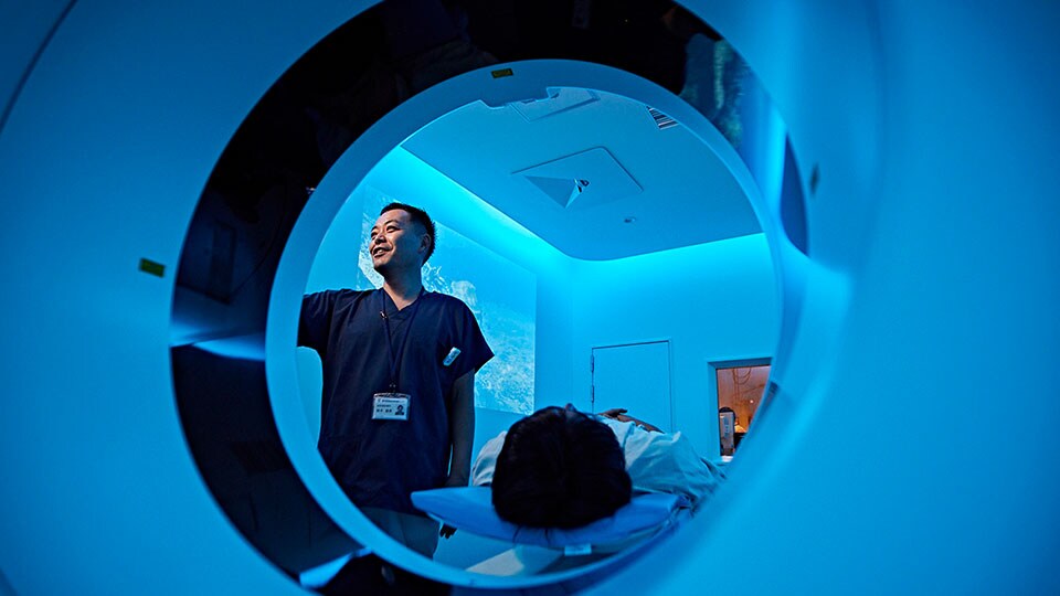 Foto van arts die een scan instelt bij het portaal van de CT-scanner, met de patiënt op de patiënttafel van het CT-systeem