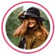 Profielfoto van reviewer, een roodharige vrouw met zwarte hoed die glimlacht.