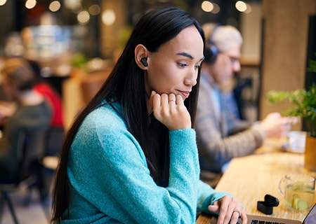 Vrouw zit in een koffieshop en gebruikt de Philips T3508 draadloze hoofdtelefoon met ruisonderdrukking