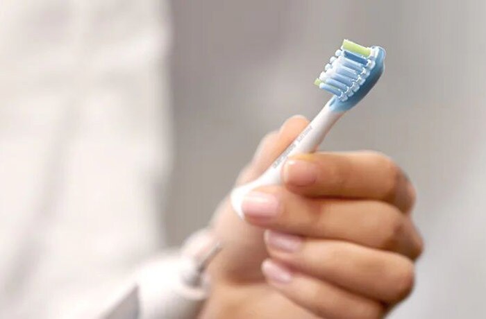 Een persoon bevestigt de afneembare opzetborstel van een witte elektrische tandenborstel.
