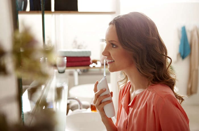 Een jonge vrouw kijkt naar haar spiegelbeeld terwijl ze haar tanden poetst met een elektrische tandenborstel.