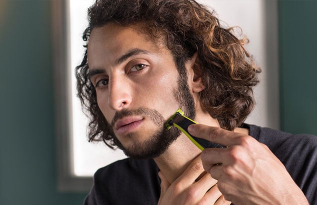Een man scheert verticaal een stukje van zijn baard en begint deze vorm te geven in een sikje.