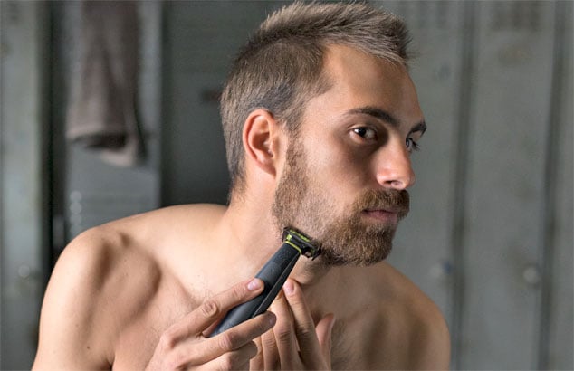 Een man trimt zijn warrige baard tot een stoppelbaardje met behulp van een trimmer met een speciaal opzetstuk.