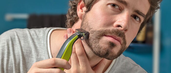 Een man trimt zijn baard een klein beetje met behulp van een trimmer met een speciaal hulpstuk.