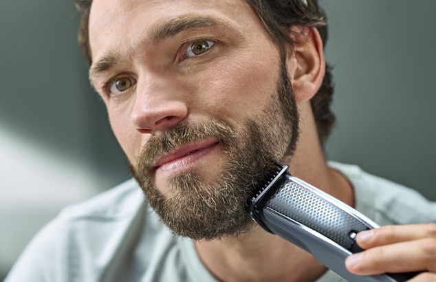 Een man met een volle baard scheert zijn gezicht met een Philips OneBlade scheerapparaat.