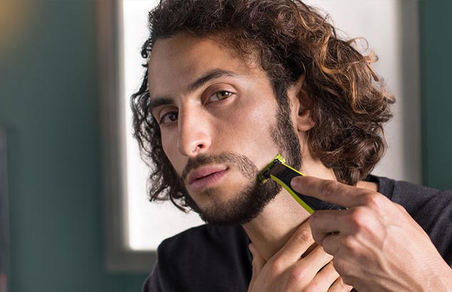 Een man scheert een deel van zijn stoppelige baard strak, waardoor een gevormde snor ontstaat.