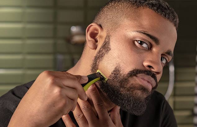 Een close-up van een man die zijn korte baard verticaal scheert, met als resultaat een gladgeschoren strook op zijn wang.
