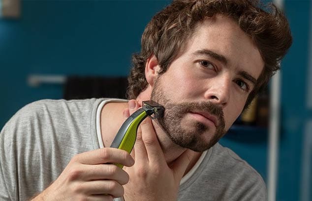 Een man trimt zijn korte kinbaard met behulp van een trimmer met een speciaal hulpstuk.