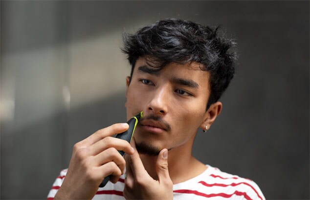 Een jongeman in een rood-wit gestreept T-shirt trimt zijn snor met de Philips OneBlade
