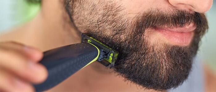 Close-up van een bruinogige man die zijn donkere baard scheert en trimt met de Philips OneBlade