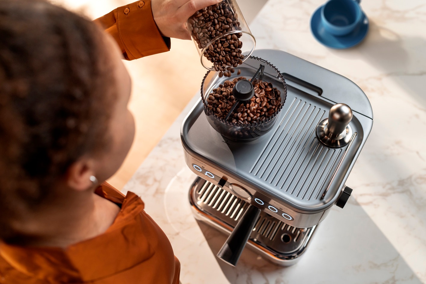 Une jeune femme verse des grains de café dans le bac à grains de la Philips Barista Brew.